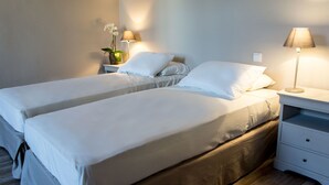 Een hotelkamer met twee bedden, een nachtkastje met een lamp en een klein tafeltje met een bloemetje.