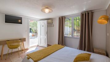 Ein Schlafzimmer mit Bett, Schreibtisch, Stuhl, Fernseher und einem Fenster mit Vorhängen.