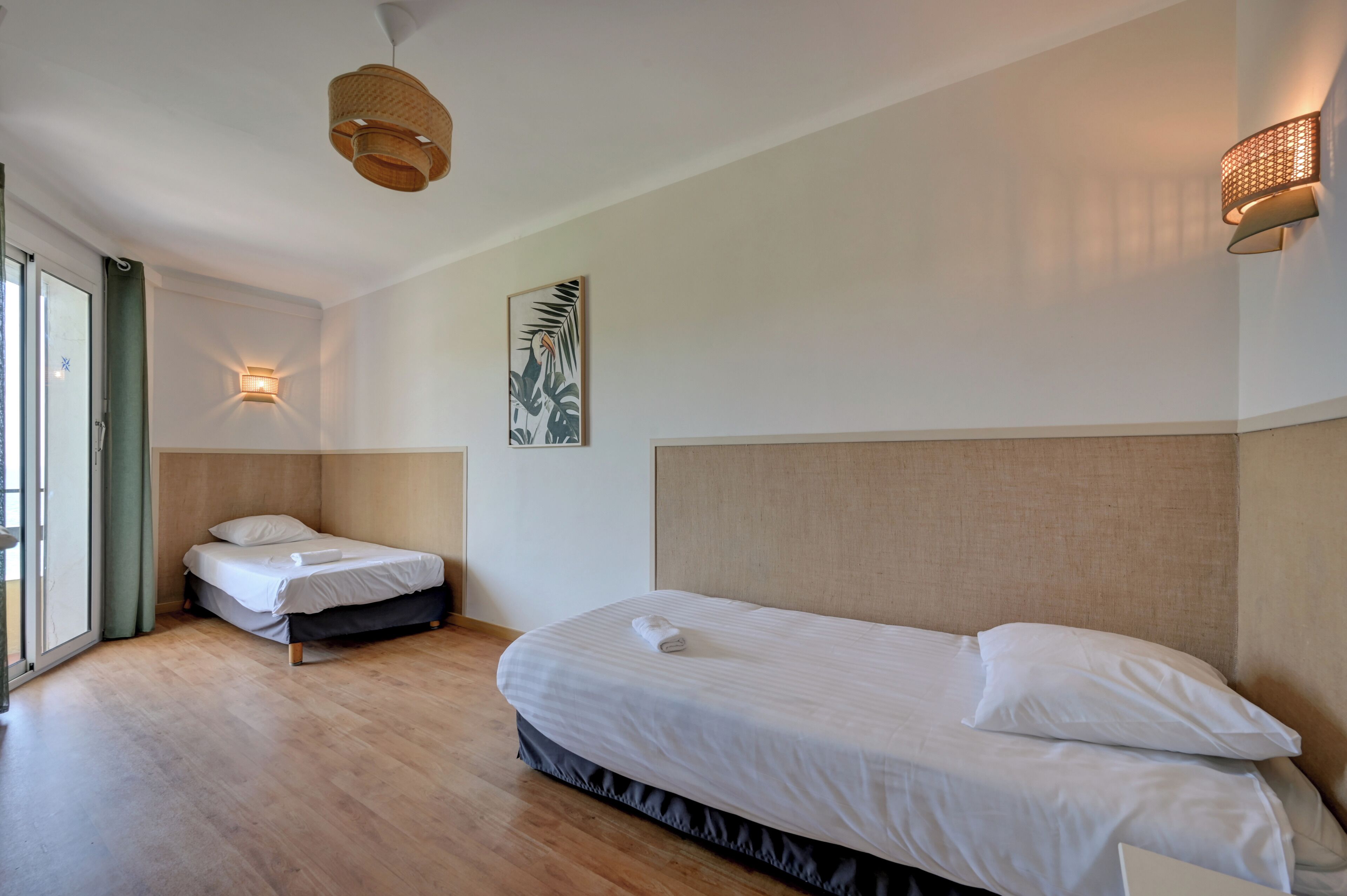 Een hotelkamer met een groot bed, een kleiner bed, een wandlamp en een plafondlamp.