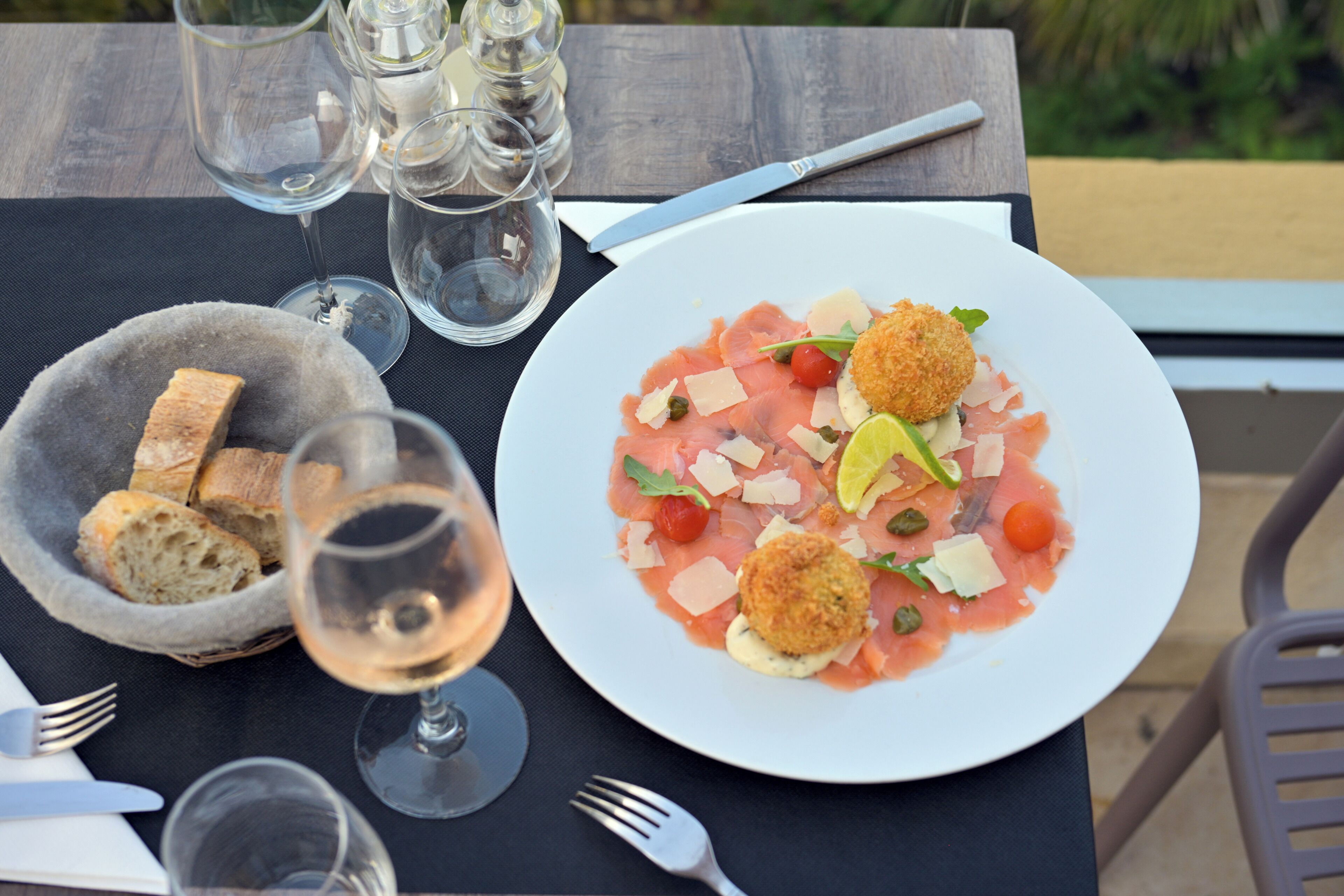 A table with a plate of food, wine glasses, and a basket of bread.