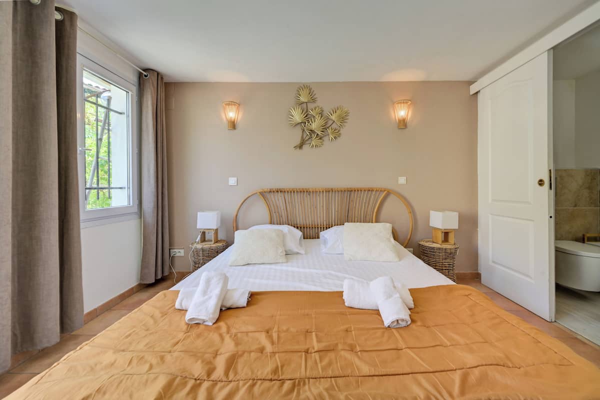 Une chambre dotée d’un grand lit, de deux lampes de chevet, d’un élément décoratif fixé au mur et d’une porte donnant accès à une salle de bain.