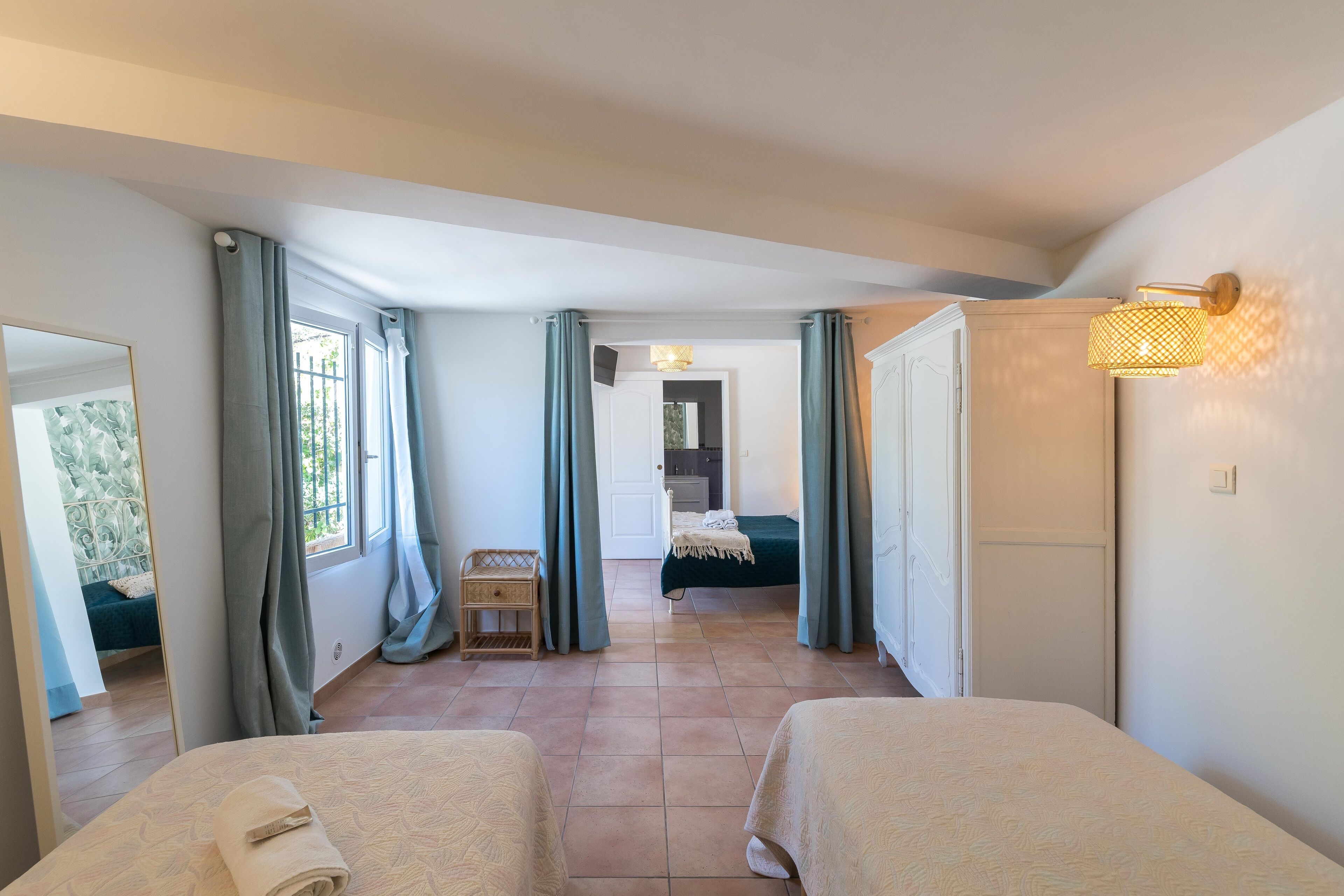A hotel room with two beds, a small table, a mirror, and a view of the hallway.