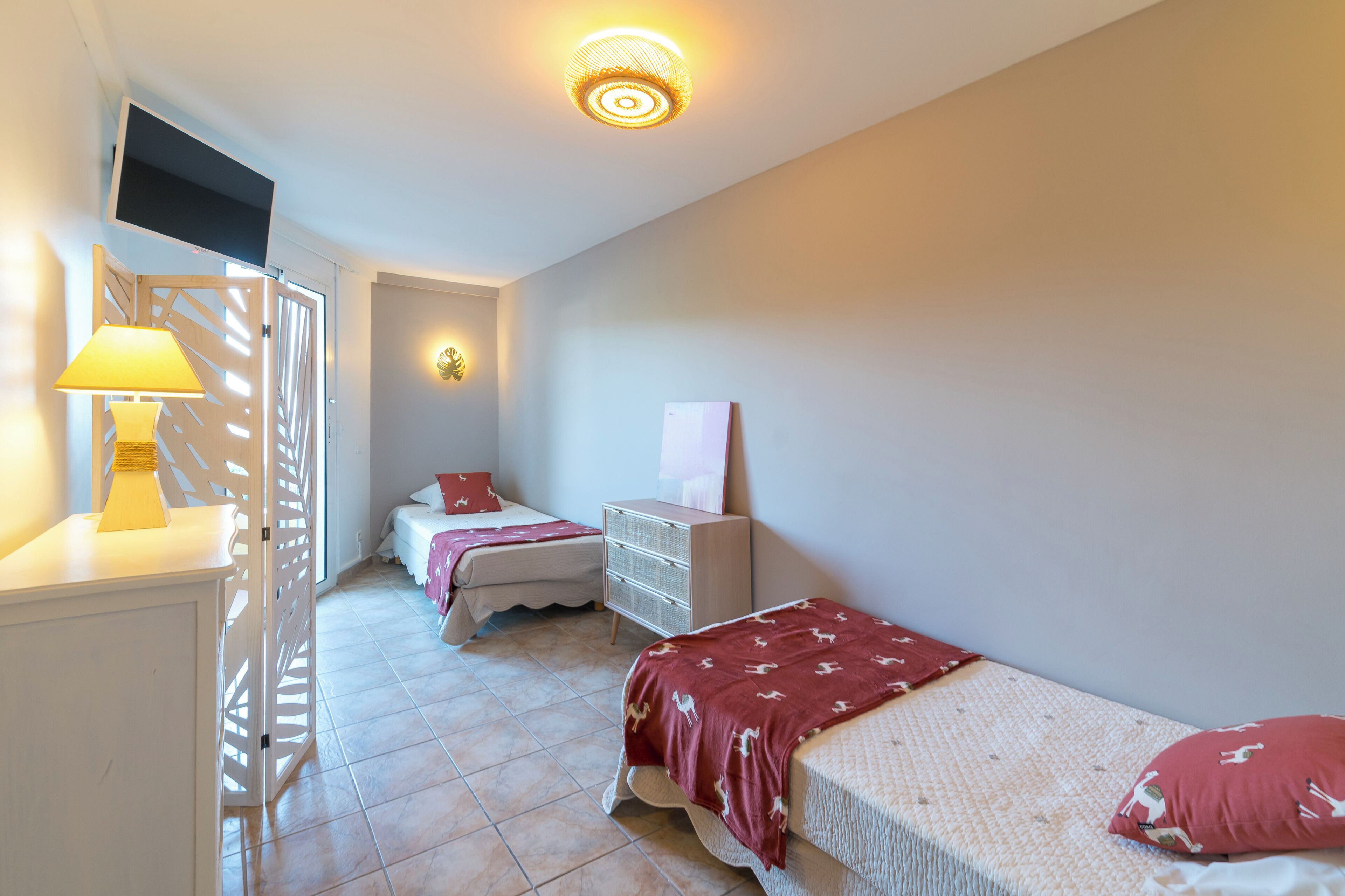 A bedroom with two beds, a dresser, a TV, and a lamp.