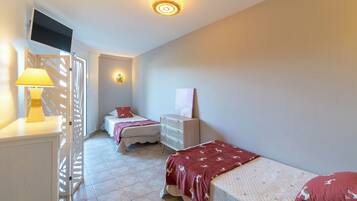 A bedroom with two beds, a dresser, a TV, and a lamp.