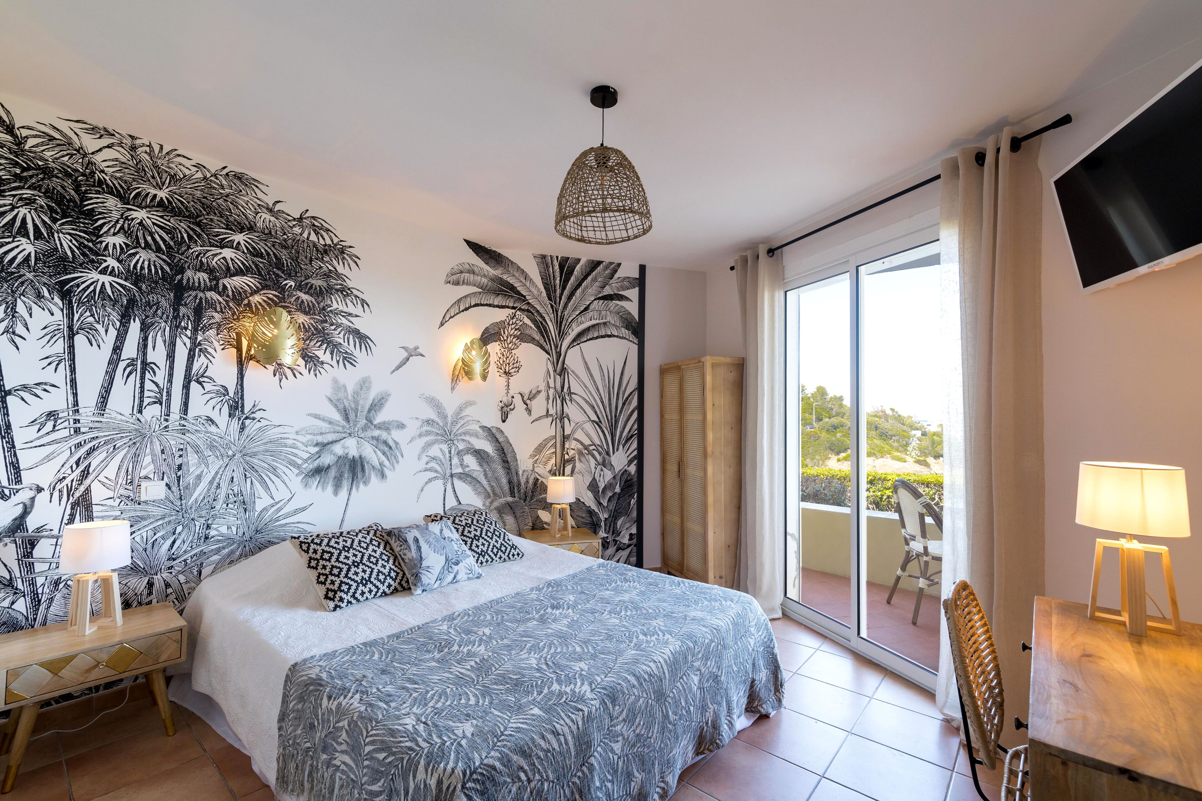 A bedroom with a bed, a nightstand, a lamp, a chair, a TV, and a balcony with a view.
