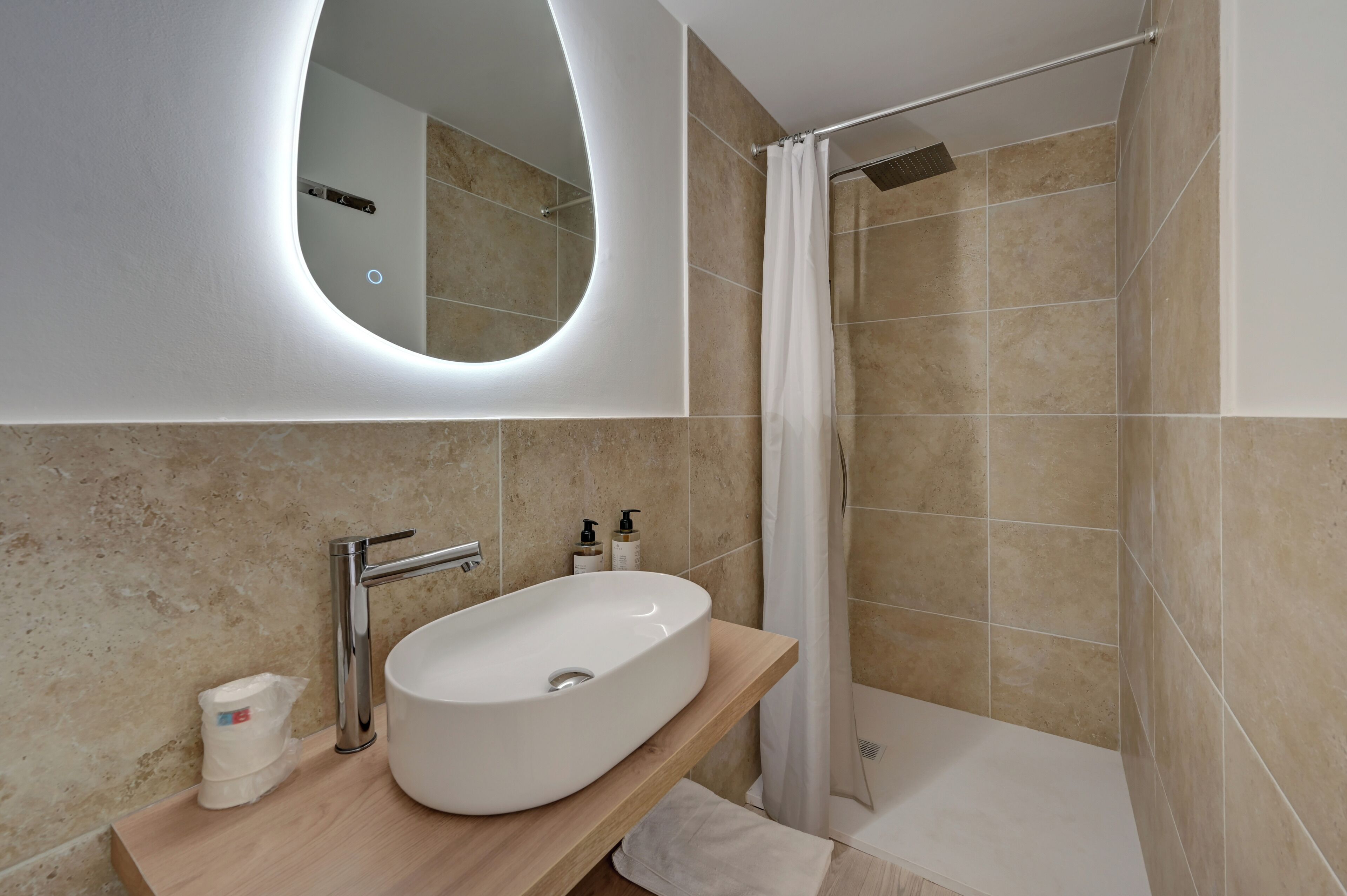 Un baño moderno con un lavamanos ovalado grande, un espejo y una zona de ducha.