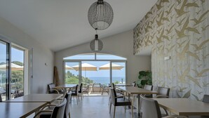 Uma sala de jantar espaçosa com pé direito alto, janelas grandes e vista para o mar.