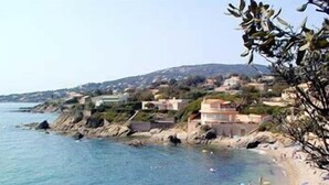 Uma praia costeira com águas cristalinas, pessoas nadando e tomando sol, e edifícios ao fundo.