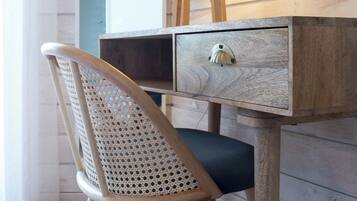 A wooden desk with a lamp, a chair with a woven backrest, and a drawer.