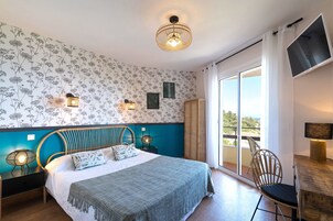 Un dormitorio con cama, una silla, un escritorio, un balcón con vistas y una pared con papel tapiz floral.