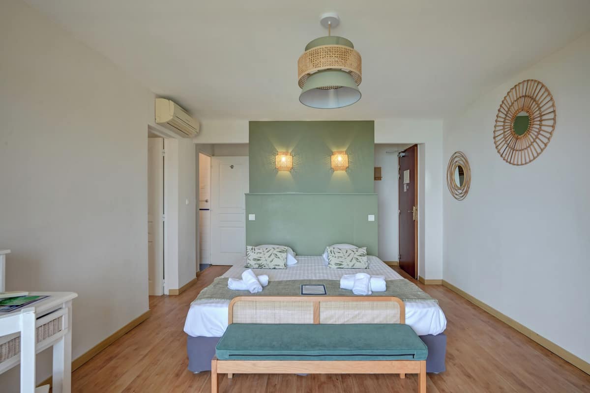 Une chambre bien rangée, avec un lit, des tables de chevet, un banc et un luminaire suspendu.