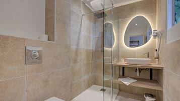 Un baño moderno con ducha envuelta en vidrio, un lavamanos blanco y un espejo grande.