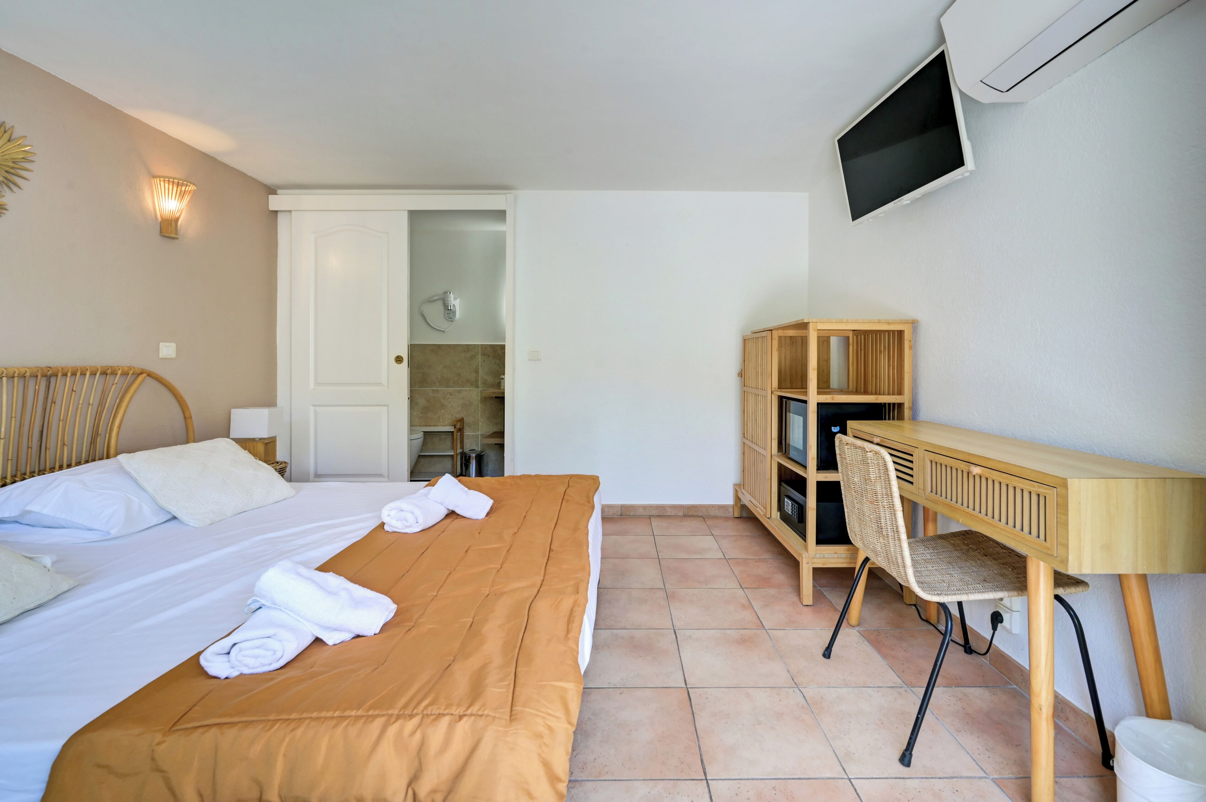 A hotel room with a bed, a desk, a chair, a TV, and a wardrobe.