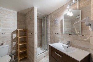 Un baño moderno con ducha de vidrio, estante de madera, lavamanos blanco y espejo con secador de pelo.