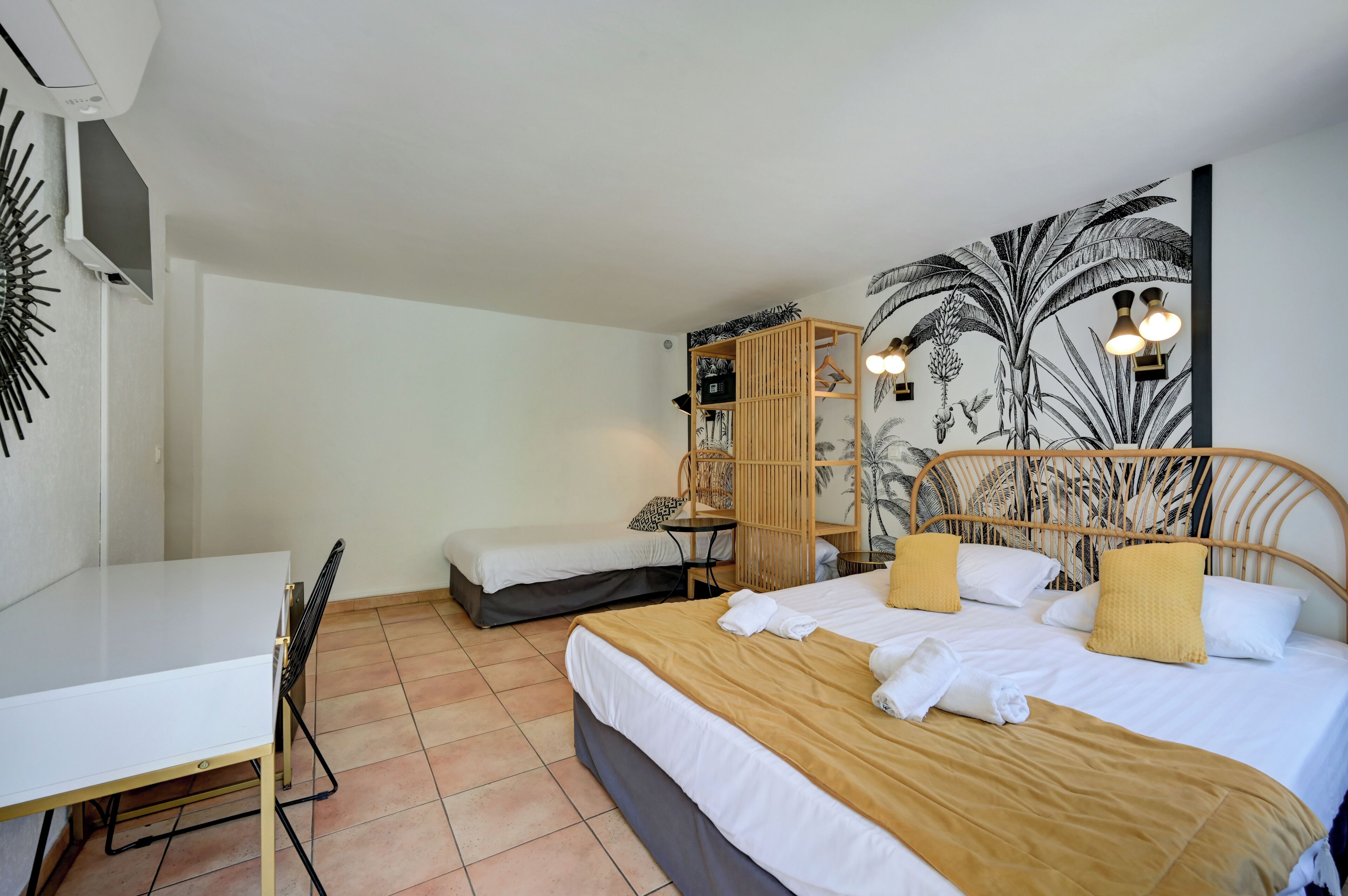 Un dormitorio con cama, escritorio, silla, armario y una pared con un mural tropical.