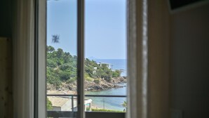 Vista pela janela de uma área costeira com edifícios, árvores e uma praia.