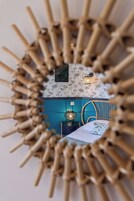 A circular mirror with a bamboo frame, a wall with floral wallpaper, a blue accent wall, and a bed with a white bedspread.