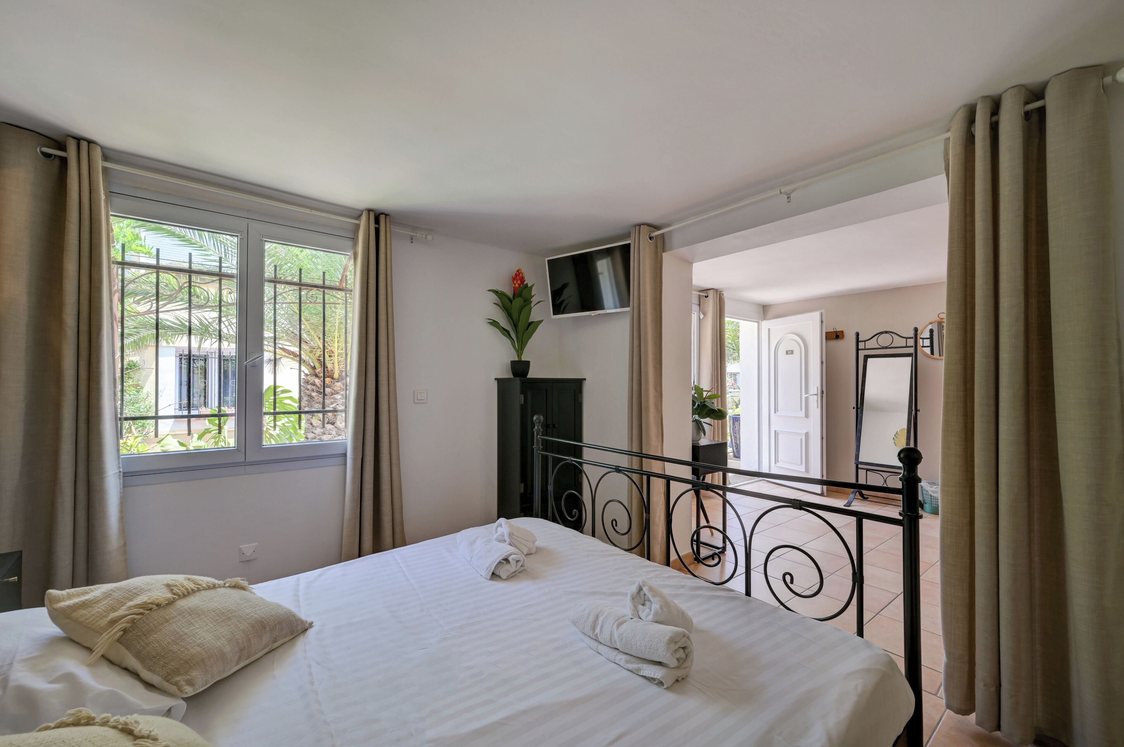 Habitación de hotel con cama, televisor, planta en maceta y vistas al exterior.