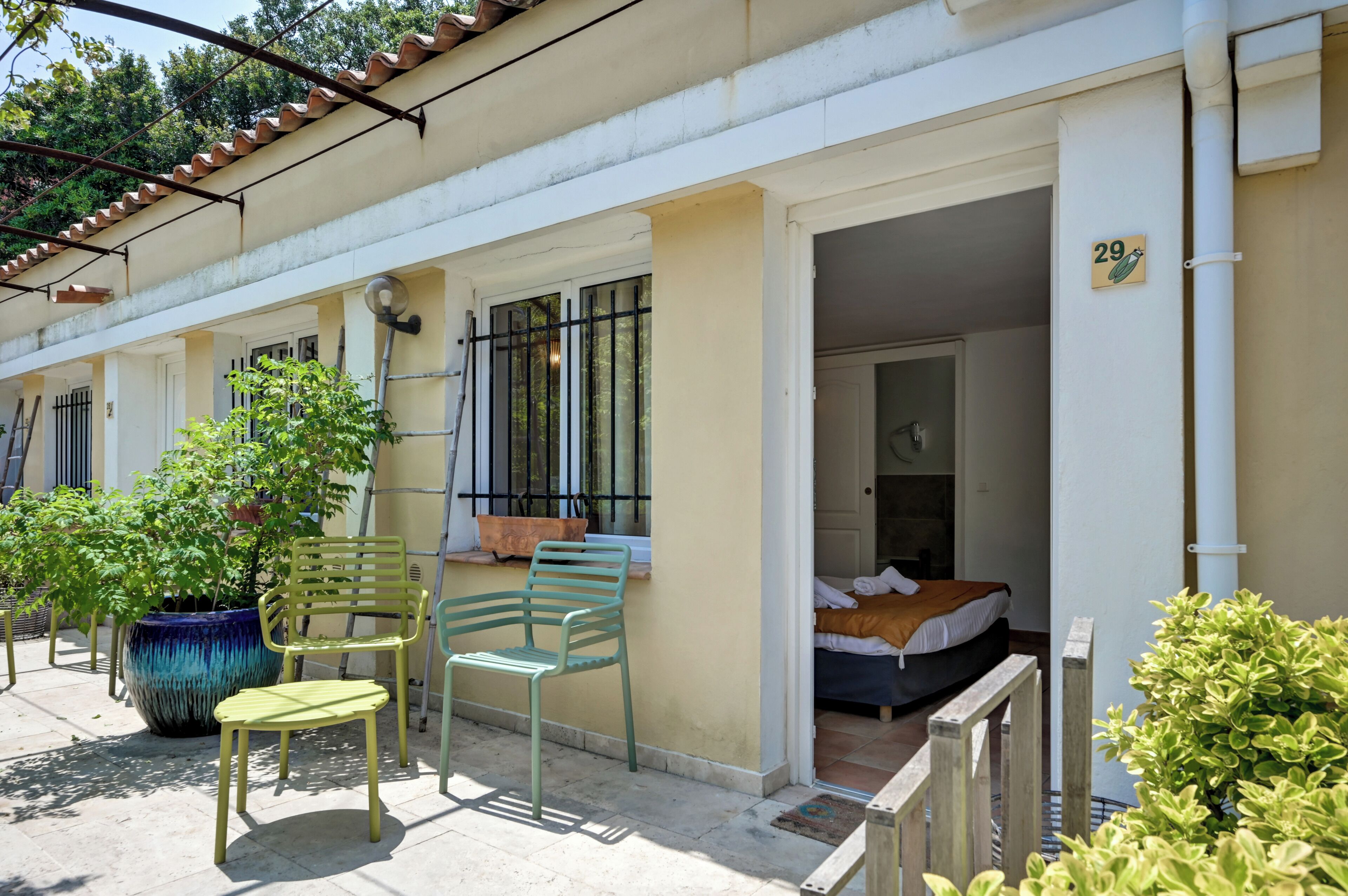 Un immeuble résidentiel doté d’un balcon, de plantes en pot et d’un lit visible à l’intérieur.