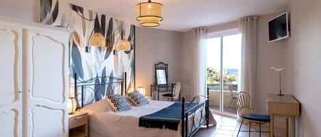 A bedroom with a bed, bedside table, lamp, chair, desk, and a TV on the wall.