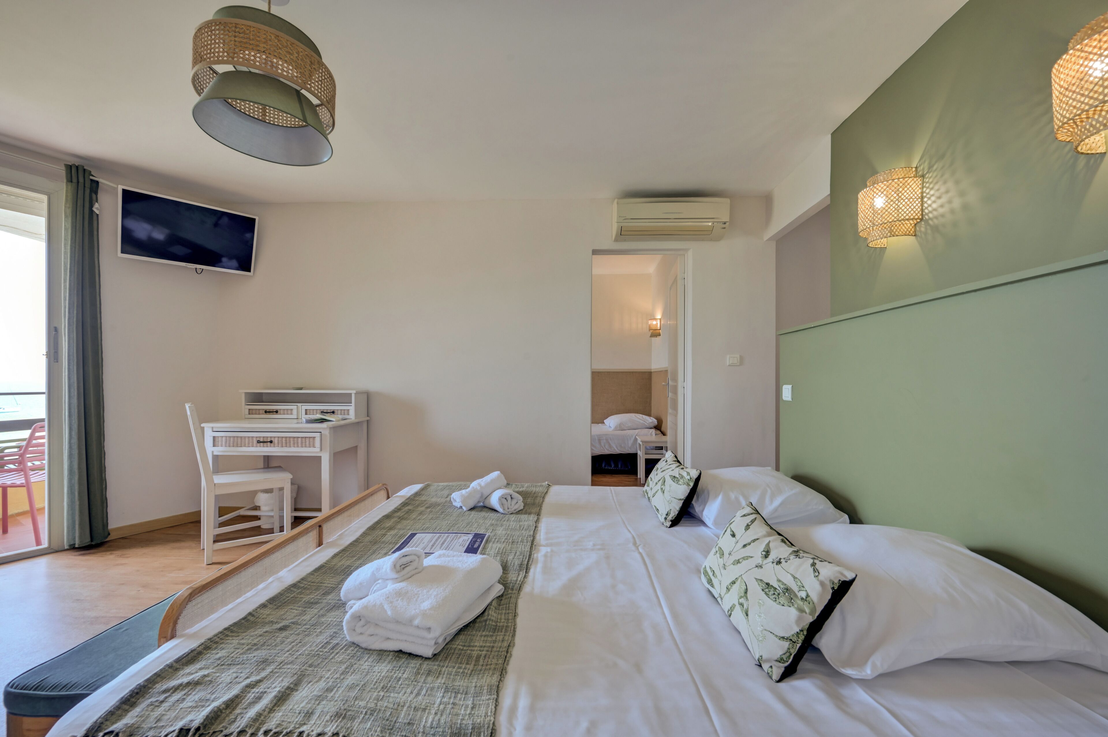 A hotel room with a bed, a desk, a chair, a television, and a balcony.