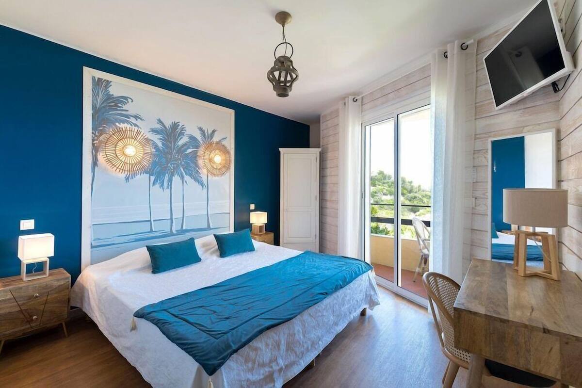 Une chambre à coucher comprenant un lit, un bureau, une chaise, une télévision et un balcon avec vue.