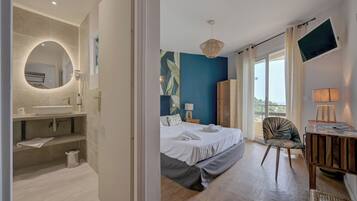 A modern hotel room with a large bed, a bathroom with a round mirror, a TV, and a view of the outdoors.