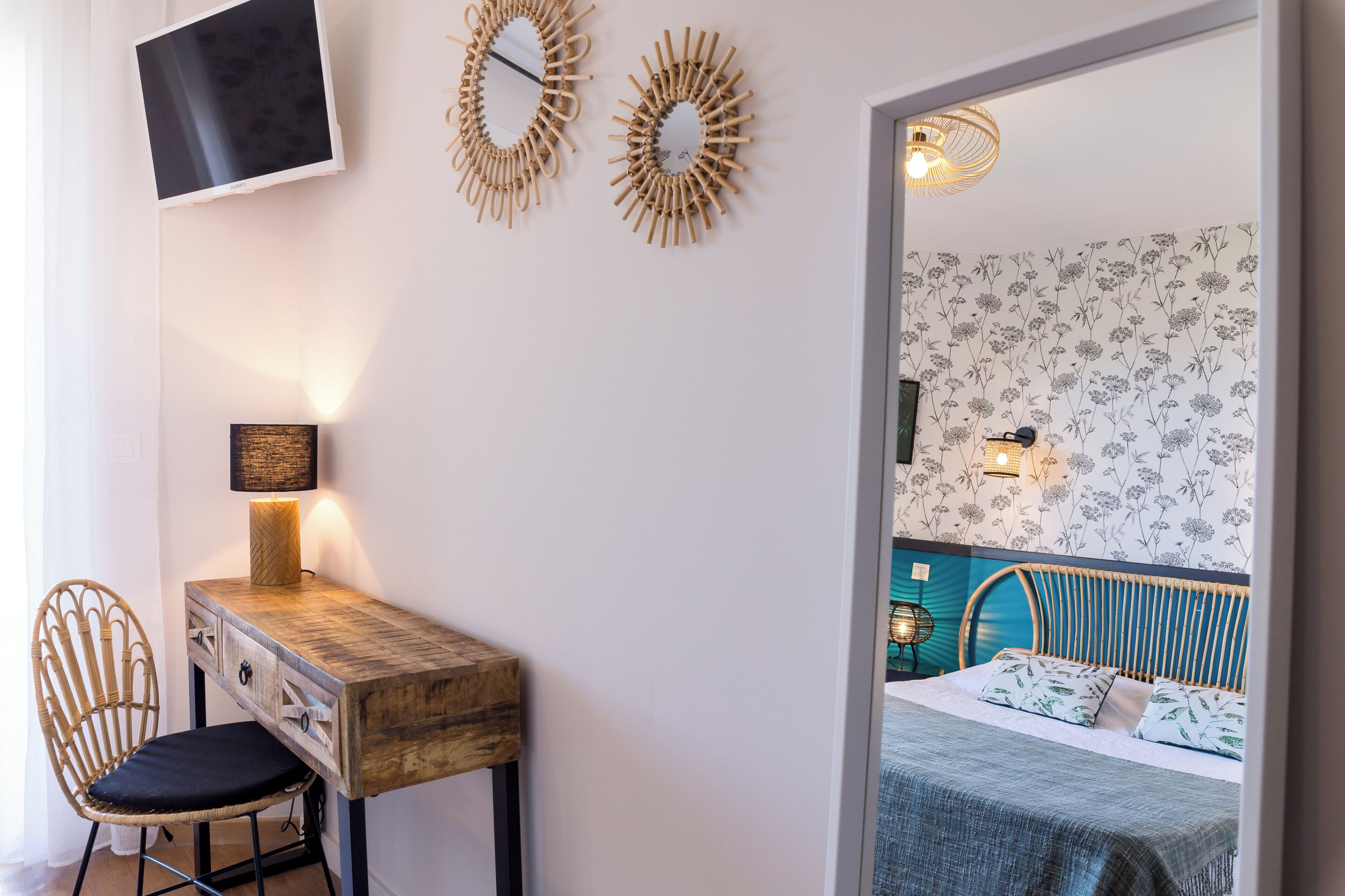 A room with a wooden desk, a chair, a bed with a blue headboard, and two wall-mounted mirrors.