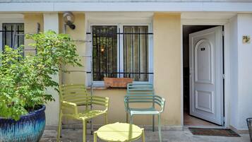 Un petit espace extérieur aménagé avec deux chaises et une table, un pot de fleurs et une porte portant le numéro 29.