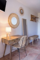 Un escritorio de madera con una silla trenzada, una lámpara de pie y adornos en la pared, incluyendo un espejo y un diseño con forma de sol.