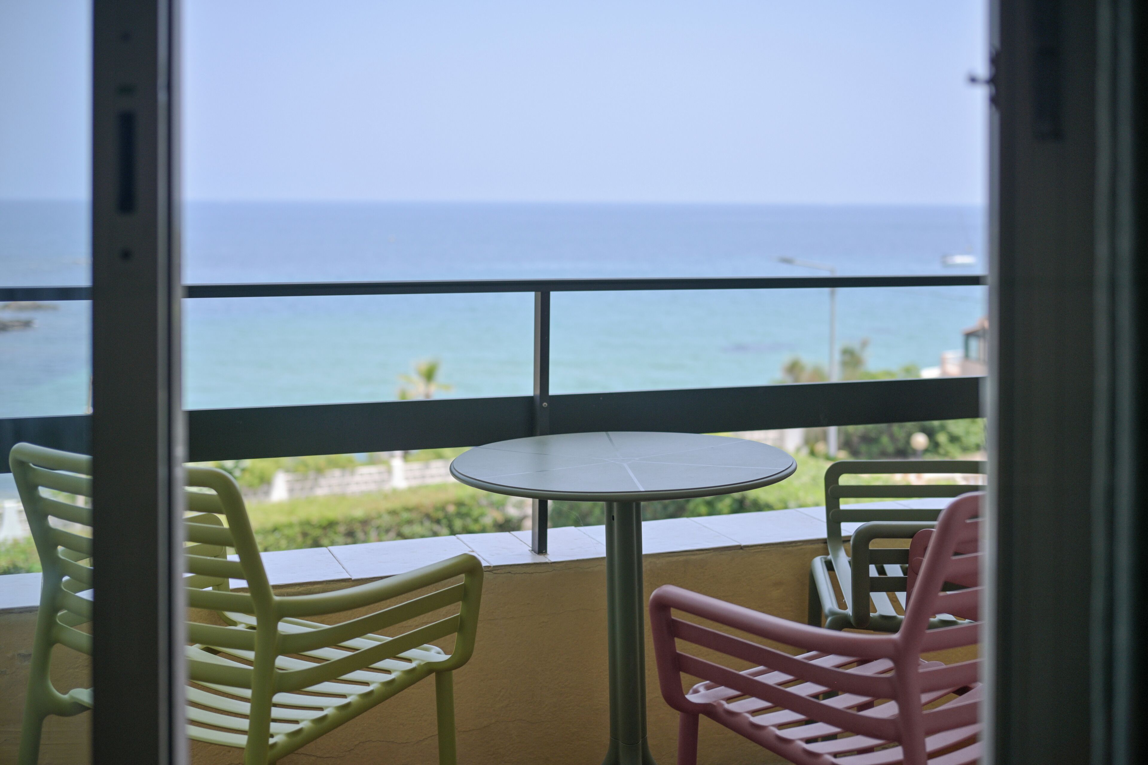 A balcony with a table and chairs, overlooking the sea.