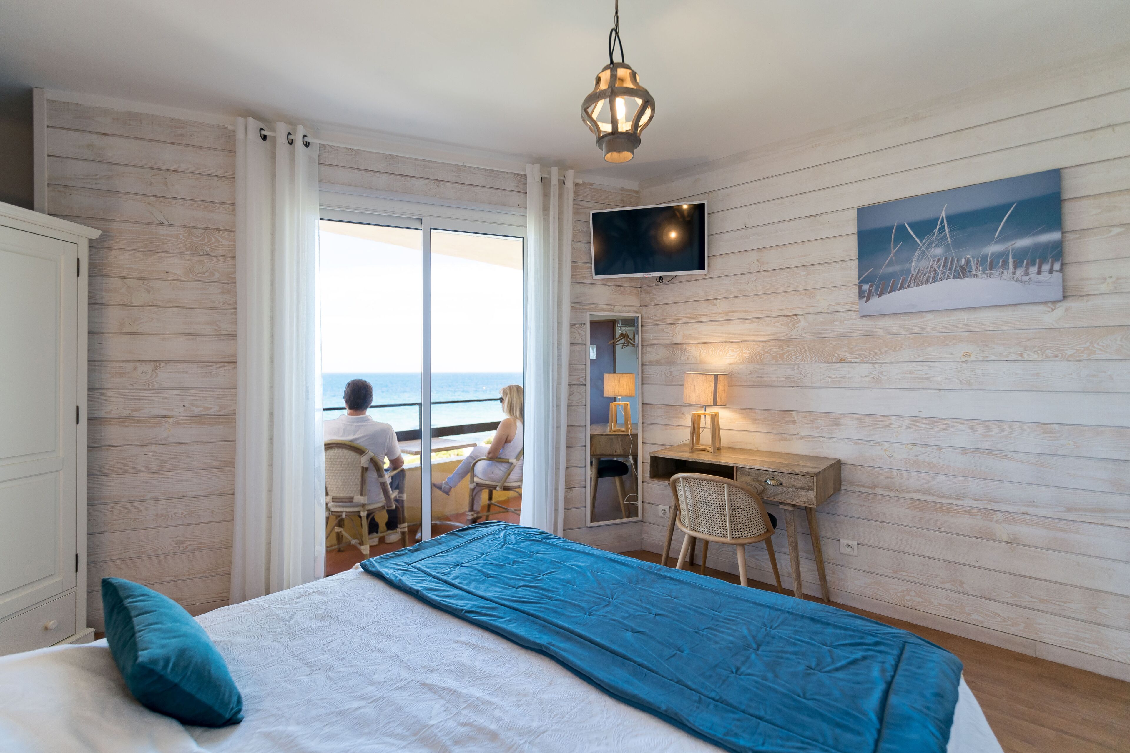 Una habitación con cama, escritorio, silla, televisor y vista al mar.