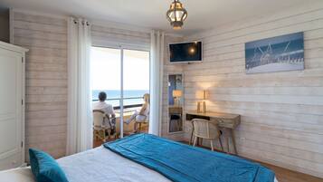 Una habitación con cama, escritorio, silla, televisor y vista al mar.