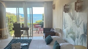 Quarto de hotel com cama, escrivaninha, cadeira e vista para o mar.
