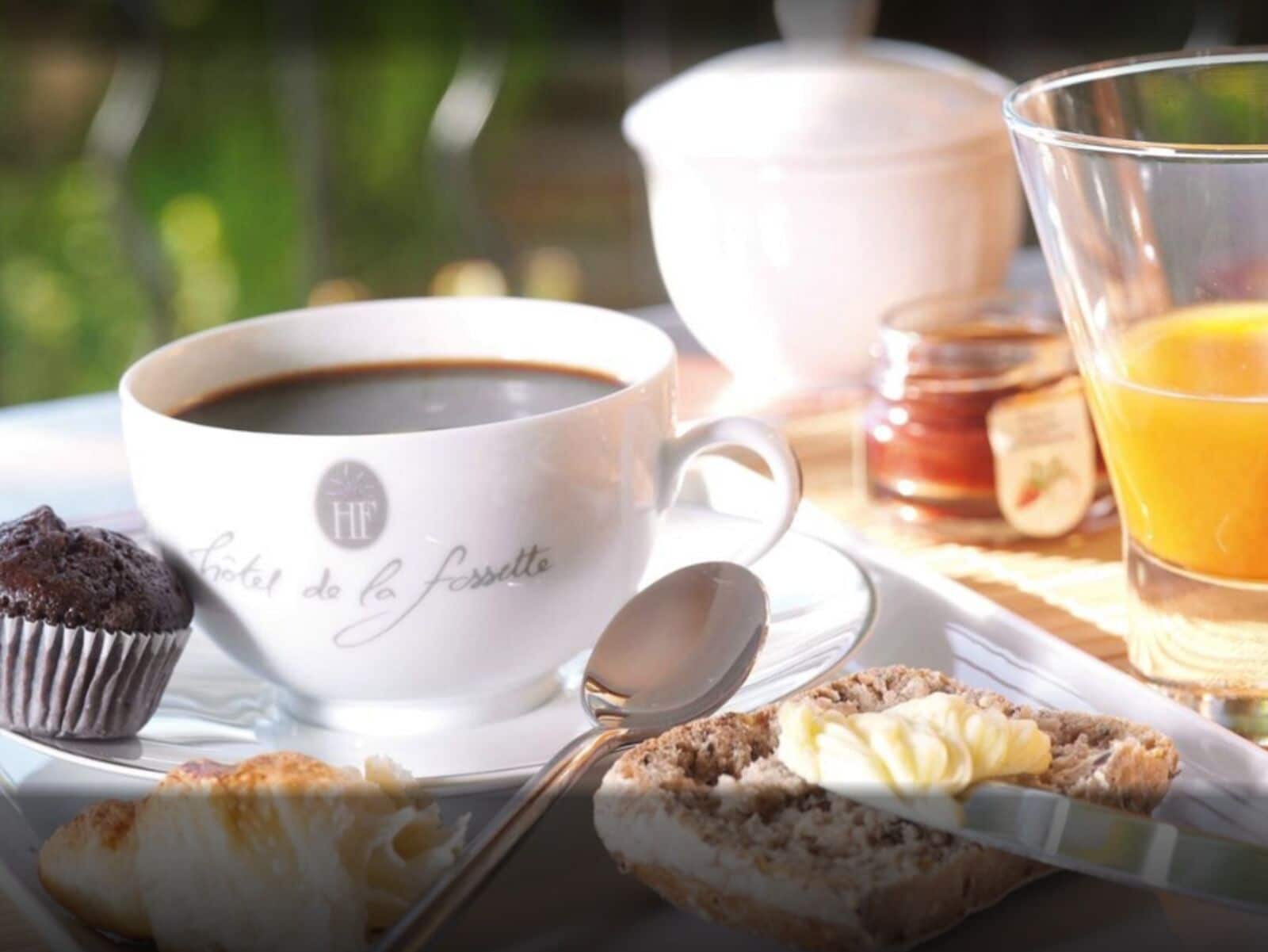 Un desayuno con una taza de café, un muffin, un pastel y un vaso de jugo de naranja.