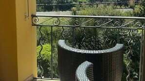 Een balkon met rieten meubilair, een metalen hekwerk en uitzicht op zee en groen.
