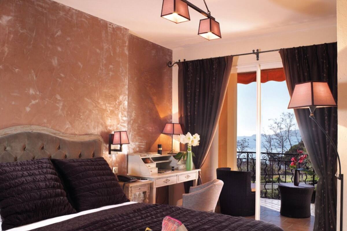 Une chambre à coucher avec un lit, des lampes de chevet, un bureau et une vue sur l’extérieur.