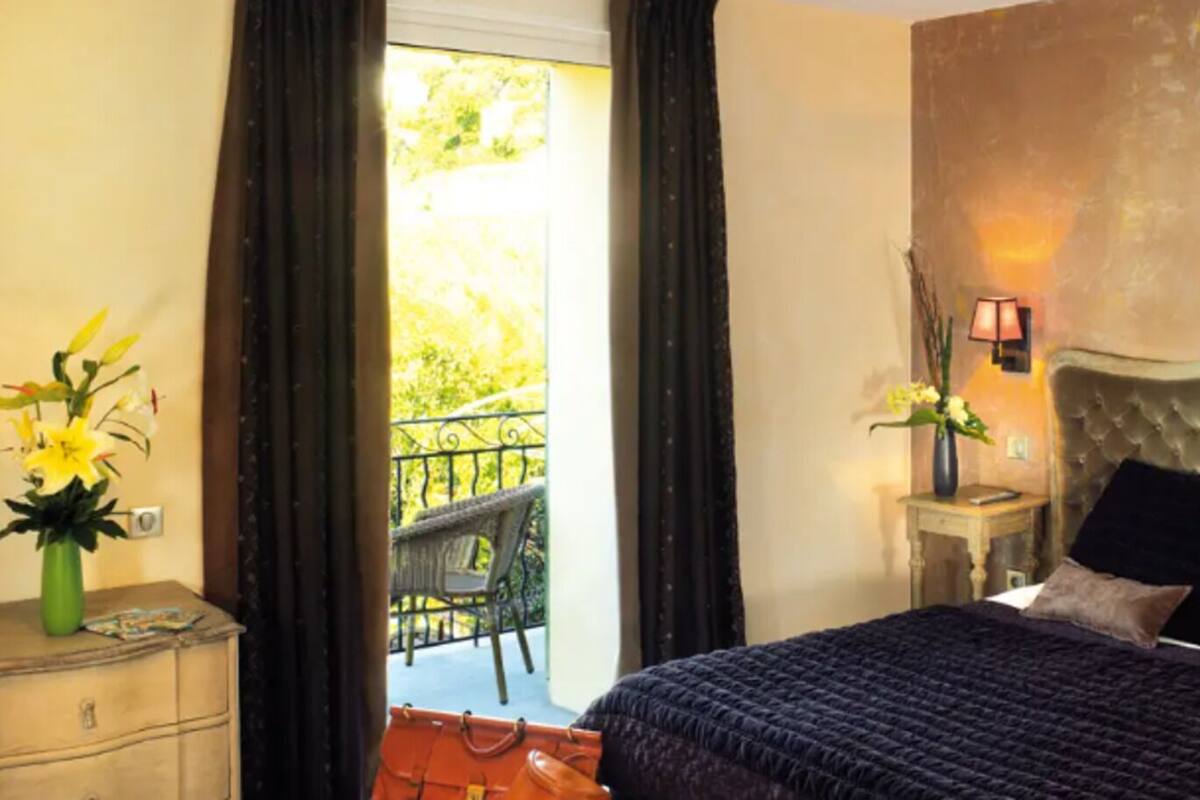 Une chambre à coucher avec un lit, une table de chevet, un vase de fleurs, une lampe et une vue sur un balcon avec une chaise.