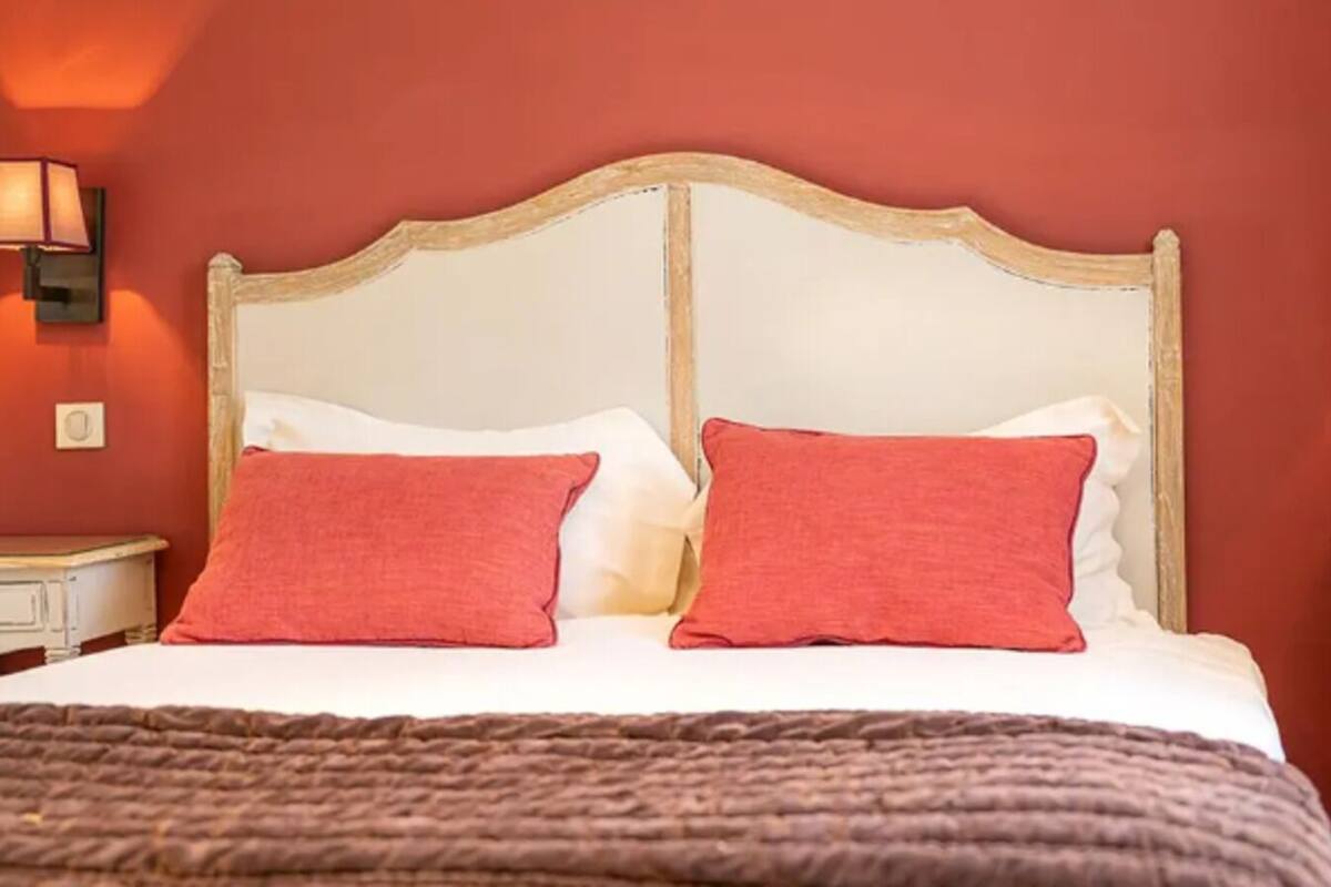 Un lit avec une tête de lit blanche et deux oreillers rouges, une couverture marron et deux tables de chevet avec des lampes.