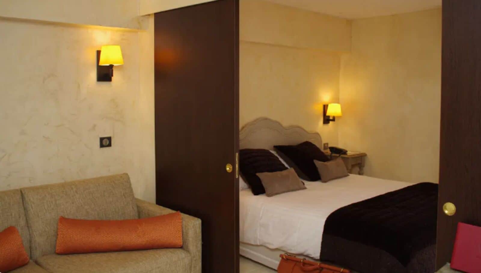Une chambre d’hôtel avec un lit, un canapé et deux lampes fixées au mur.