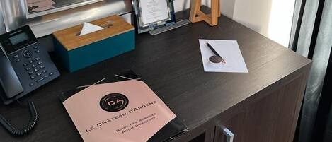 Escritorio de habitación de hotel con un teléfono, una caja de pañuelos, un cartel y una lámpara.