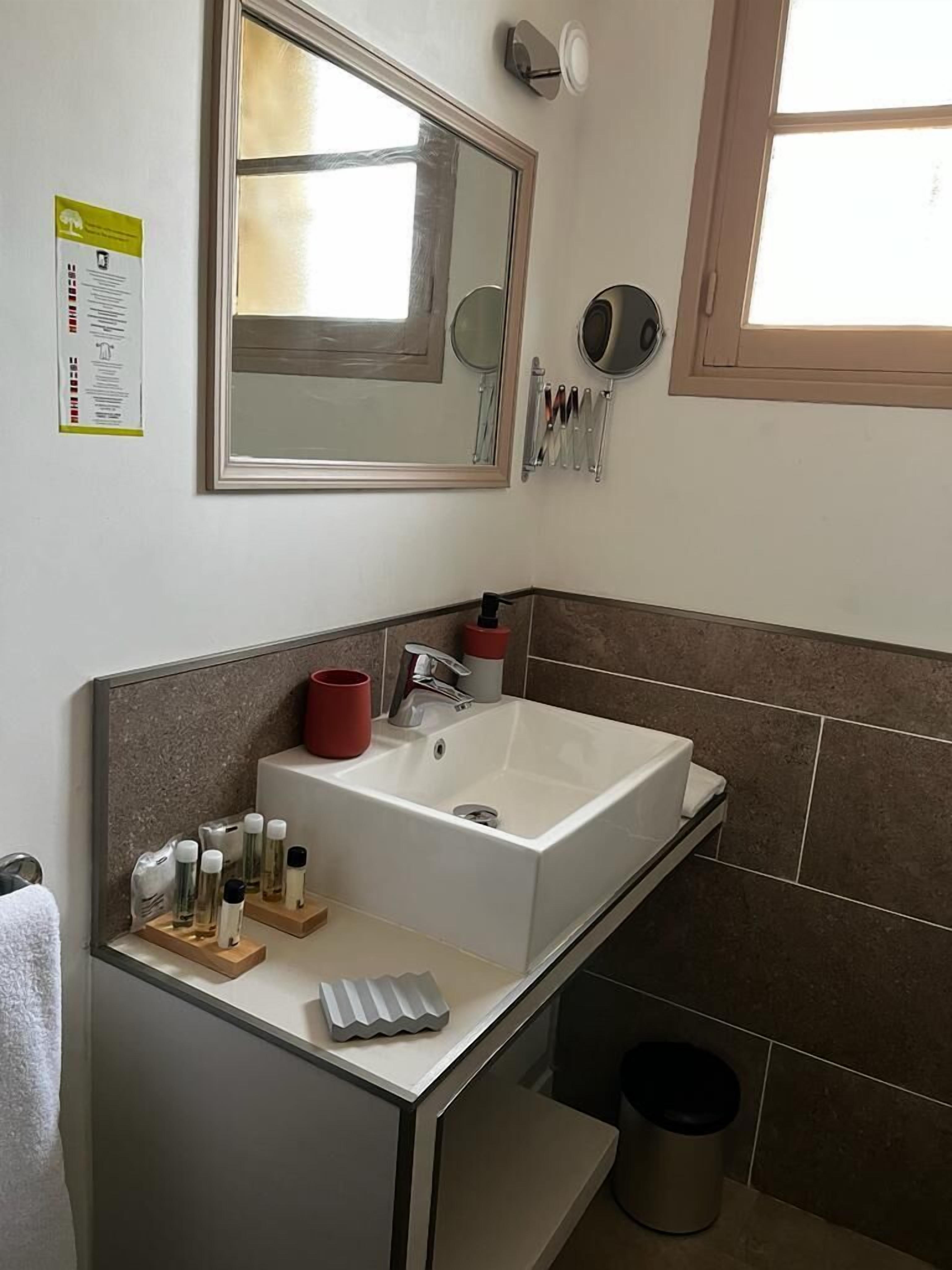 Un baño moderno con un espejo grande, un lavabo blanco y una pequeña encimera con artículos de aseo.