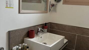 Un baño moderno con un espejo grande, un lavabo blanco y una pequeña encimera con artículos de aseo.