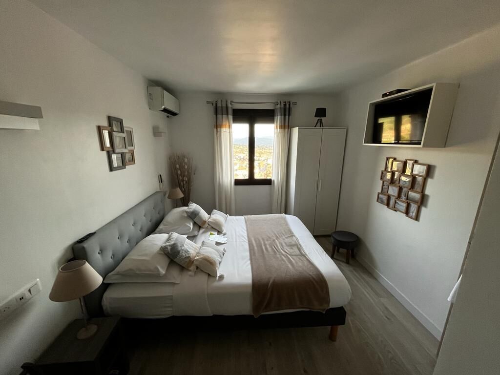 Une chambre à coucher comprenant un lit, une table de chevet, une lampe, une armoire et une fenêtre avec des rideaux.