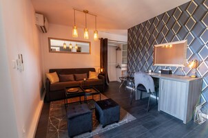 Una sala de estar moderna con sofá, mesa de centro, reposapiés y un escritorio con silla. Hay un espejo en la pared y un equipo de aire acondicionado.
