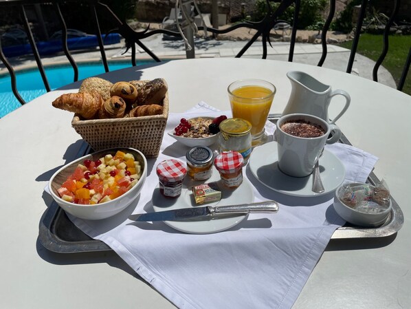 A breakfast table with croissants, fruit, cereal, orange juice, and a coffee cup by a pool. - Le Chateau d'Argens (Les Arcs-sur-Argens)