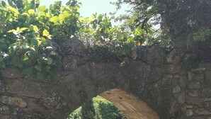 Un arc en pierre mène à une cour intérieure où se trouvent une chaise en osier et une table.