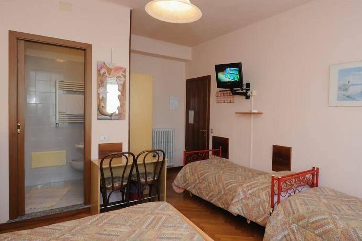 A small, cozy room with two single beds, a television mounted on the wall, and a door leading to a bathroom.