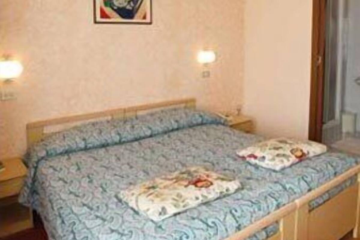 A bedroom with a bed, two bedside lamps, a wall-mounted picture, and a door.