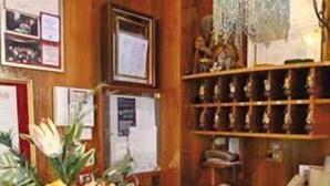 A reception area with a counter, a flower arrangement, framed pictures on the wall, and a shelf with various items. - Hotel Elena (Stresa)
